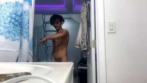 Media: A candid video of a naked person with short black hair in a modern bathroom, with a white countertop and blue shower curtain visible.