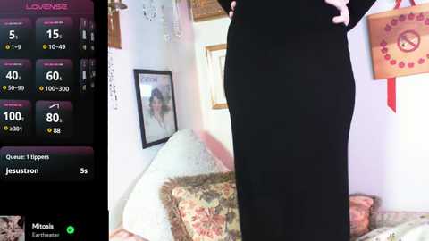 Media: Video of a person in black clothing standing near a bed with patterned pillows, a framed photo on the wall, and a colorful decorative item hanging.