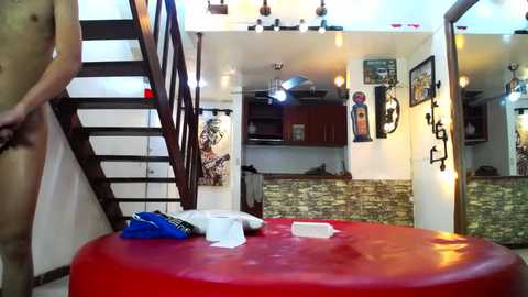 Media: Video of a modern, loft-style apartment with a red ottoman, wooden staircase, hanging artwork, exposed stone wall, and a minimalist interior.