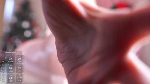 Media: A close-up video of a human foot, focusing on the toes and sole. The background is blurred, featuring a festive holiday setting with Christmas lights and decorations. The image appears to be taken with a smartphone, indicated by a digital zoom indicator.