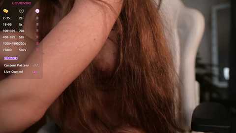 Media: A close-up video of a woman with light skin and long brown hair, partially obscured by a hand, in a dimly lit room.