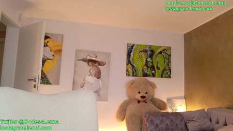 Media: A video of a modern living room featuring a beige teddy bear, two framed artworks, a white couch, and a warm-toned wall.