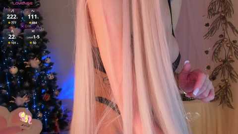 Media: Video of a woman's legs, wearing a sheer pink dress, standing beside a decorated Christmas tree.