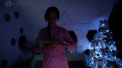 Media: A video of a young girl in a pink pajama set, holding a bag of chips, standing in a dimly lit room with a Christmas tree adorned with blue lights.