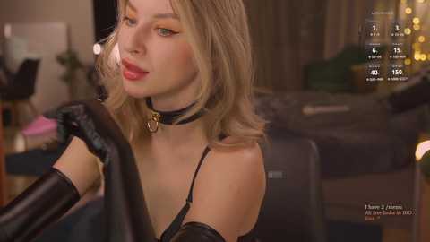 Media: Video of a blonde woman in black lingerie, holding a black leather jacket, in a dimly-lit room with blurred background.