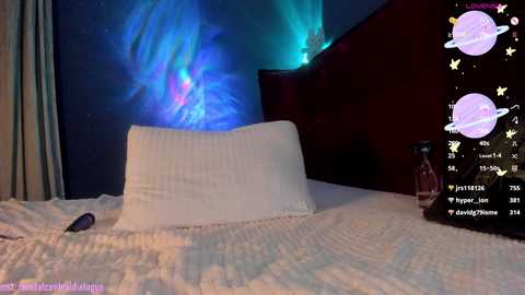 Media: Video of a dimly lit bedroom with a white bed, a pink pillow, and a red headboard, featuring a glowing, blue, aurora borealis-themed wallpaper.