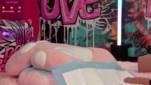 Media: Video of a person in a white furry suit with blue accents, lying on a bed covered in white fur, against a colorful graffiti wall with \"LOVE\" written in bold letters.