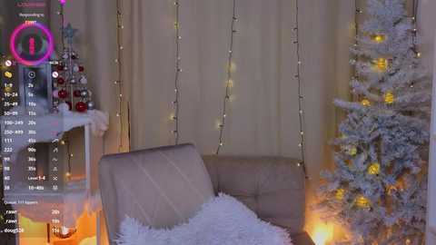 Media: Video of a cozy living room with a beige sofa, snow-covered Christmas tree, and twinkling fairy lights. Background shows a fireplace with a mantle holding ornaments.