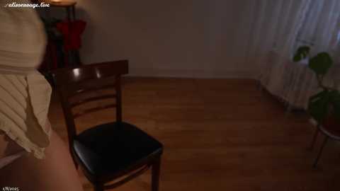 Media: A video of a dimly-lit bedroom with a wooden floor, a black chair, a beige bed, and a lamp on a nightstand. The room has a simple, cozy atmosphere.