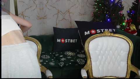 Media: Video of a festive living room with a green couch, gold-framed chairs, a decorated Christmas tree, and \"MSTERB\" pillows.