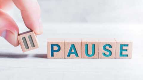 Media: Video of a light-skinned hand holding a wooden block with the letter \"P\" in blue, placing it on a stack of similarly colored blocks spelling \"PAUSE.\" The background is a soft, blurred white.