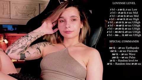 Media: Video of a tattooed, light-skinned woman with shoulder-length blonde hair, wearing a beige halter top, sitting in a dark room, holding a phone to her ear. Text overlays show game stats.