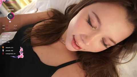 Video of a young, light-skinned woman with brown hair, lying on a bed, wearing a black top, with a serene expression.