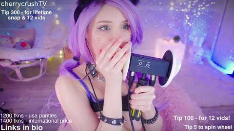 Media: Video of a young woman with purple hair, wearing black lingerie and a spiked collar, holding a microphone, in a cozy bedroom with a glittery background. Text overlays mention her social media and tips.