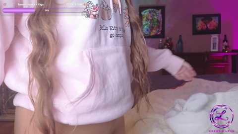 Media: Video of a woman in a white hoodie, with long blonde hair, standing in a bedroom with pink walls, a framed photo, and a TV showing a couple.