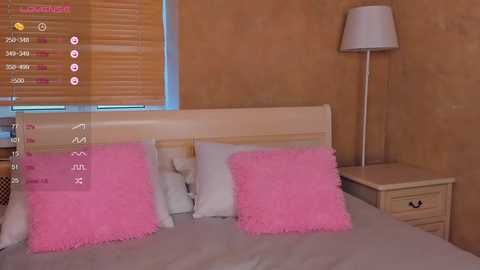 Video of a cozy bedroom with a light wooden bed, two pink fluffy pillows, a beige wall, and a white lamp on a matching nightstand.