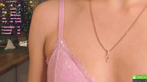 Media: Video of a fair-skinned woman's bare upper back and shoulders, wearing a delicate, pale lavender lace bra and a gold necklace with a heart pendant, in a softly lit indoor setting.