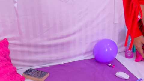 A video of a colorful indoor scene with a purple exercise ball, a calculator, a mouse, and vibrant red and pink clothes hanging on a white wall.