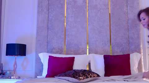 Media: Video of a modern bedroom with a gray upholstered headboard, two red pillows, a leopard-print cushion, a black lamp, and a white wall.