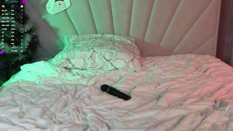 Media: Video of a bed with white bedding, a black dildo on the bedspread, a plush pillow with a cartoon character, and a Christmas tree in the background, with green and red lights.