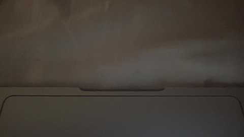 Media: A video of a dimly lit, worn, beige wall with a textured surface and a faint, vertical line at the bottom center. The image has a muted, monochromatic tone with minimal contrast.