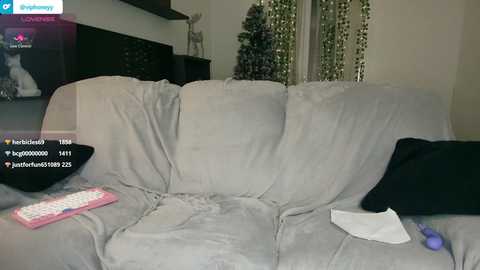 Media: Video of a plush, light gray sofa with a black cushion and a pink remote control, in a living room with a TV and a Christmas tree.