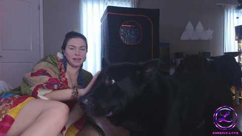 Media: Video of a smiling woman in a floral kimono petting a black dog in a dimly lit room with a retro stereo and window with white curtains.