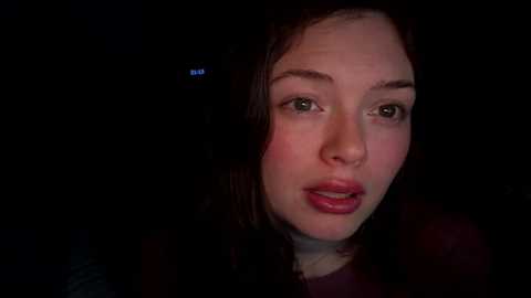 Media: A video of a Caucasian woman with fair skin, dark hair, and green eyes, wearing red lipstick, against a dark background.