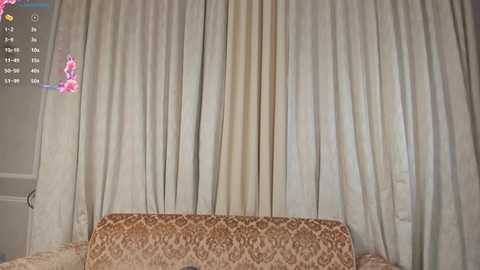 Media: A video of a beige curtain with a white floral pattern, hanging in front of a patterned, brown sofa. A digital overlay shows a clock and weather information.