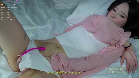 Media: A video of an East Asian woman with pale skin, lying on a bed, wearing a pink robe, white underwear, and a pink vibrator. She appears relaxed, with soft lighting.