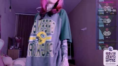 Media: A video of a person with pink hair wearing a large green and yellow \"Boston Bruins\" t-shirt, taken in a dimly lit room.