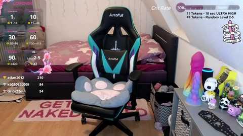 Media: Video of a gamer's room with a black and teal gaming chair, pink bedspread, toys, and plushies; game stats overlay.