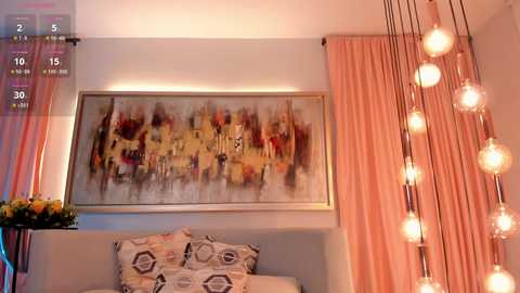 Media: Video of a modern living room with a large, abstract painting on a white wall, pink curtains, geometric-patterned pillows, and a cluster of hanging light bulbs.