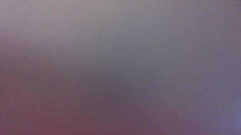 Media: A blurry video of a gray, textured surface, possibly a wall or floor, with subtle hints of pink and purple hues, creating a muted, abstract background. The image lacks distinct details or identifiable objects.