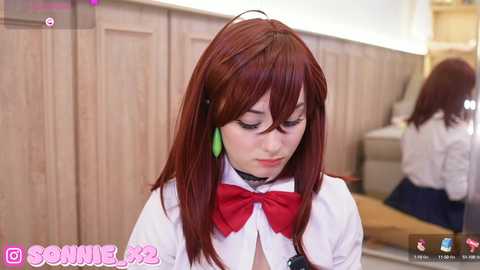 Media: Video of a young, fair-skinned woman with long, straight auburn hair, wearing a white blouse with a red bow, green earrings, and a black choker. She's in a room with wooden paneling, reflected in a mirror.