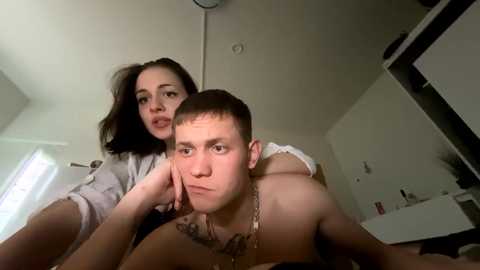 Media: Video of two people in a bedroom: a man with short hair and a necklace, leaning on his elbows, and a woman with dark hair, partially covered, leaning on his shoulder.