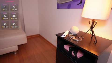 Media: Video of a minimalist bedroom with a white couch, wooden floor, black side table holding a lamp, clock, and a small white ball, featuring a purple abstract painting on the wall.