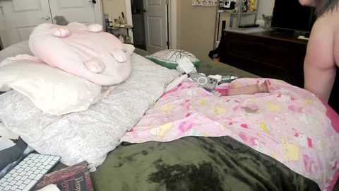 Media: A video of a messy bedroom with a woman in a pink nightgown, surrounded by plush toys, a keyboard, and a cluttered desk.