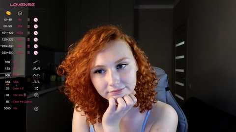 Media: Video of a young, fair-skinned woman with curly red hair, wearing a light blue tank top, sitting in a gaming chair, with a streaming platform interface in the background.