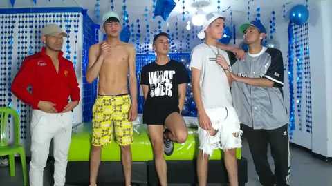 Media: Video of five young men in casual, brightly colored clothing, posing indoors with blue and white decor, including balloons and a pool table.