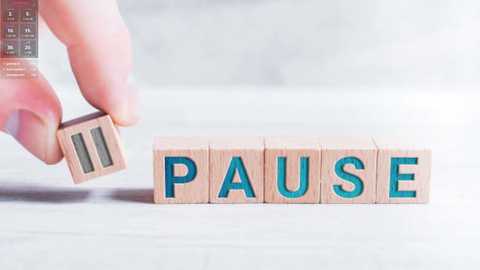 Media: Video of a hand holding a wooden block with the word \"PAUSE\" in blue letters, placed on a light-colored, textured surface.