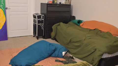 Media: Video of a messy bedroom with a black dresser, green and orange bedding, blue pillow, and a teal blanket.