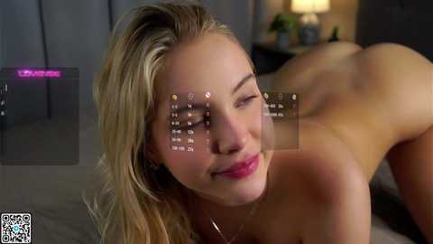 Video of a nude, fair-skinned blonde woman with long hair, lying on her stomach on a bed. She has a serene expression and her face is overlaid with virtual text.