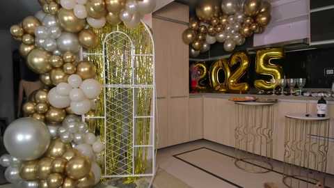 Media: Video of a modern, elegant New Year's Eve party setup with gold and silver balloons, metallic fringe, and large \"2023\" letters in gold. White bar stools and a champagne bottle are visible in the background.