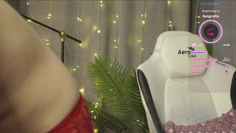 Media: A video of a woman in red lingerie leaning against a white gaming chair, surrounded by string lights and a fern, with virtual text overlays and a webcam icon.