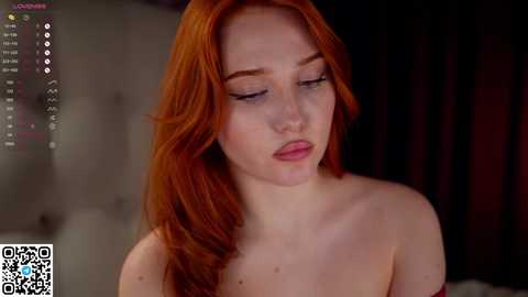 Media: Video of a fair-skinned, red-haired woman with long, wavy hair and closed eyes. She is topless, her breasts covered by a light-colored cloth. The background is dimly lit, suggesting a private, intimate setting.