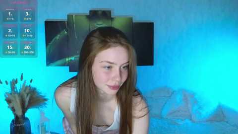 Media: Video of a young Caucasian woman with long brown hair, wearing a white tank top, in a dimly lit room with blue lighting.