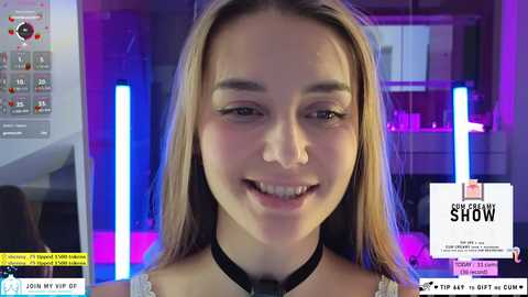 Media: Video of a young woman with straight, light brown hair and fair skin, smiling. She wears a black choker necklace. Background features a modern kitchen with purple lighting and a \"Seeking Sorrow\" promotional poster.