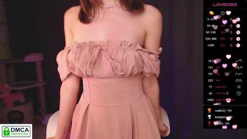 Media: Video of an East Asian woman with light skin wearing a pink off-shoulder dress, seated against a dark background. Social media icons in the right corner indicate live streaming.