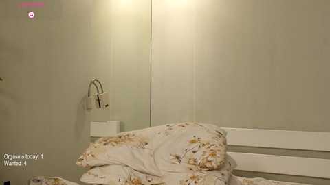 Media: Video of a minimalist, beige-tiled bathroom with a white, floral-patterned bedspread and a white chair. A wall-mounted soap dispenser and mirror are visible, creating a serene, clean atmosphere.